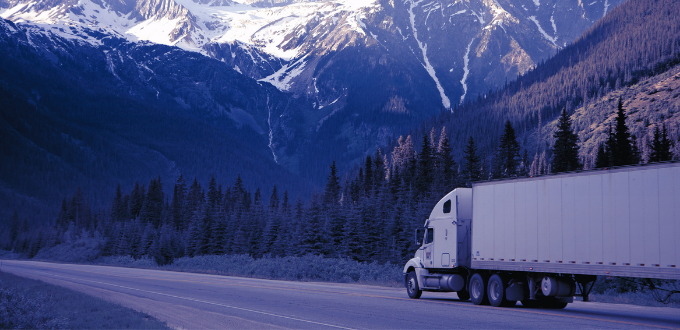 purple filtered lorry driving on road through trees and mountains